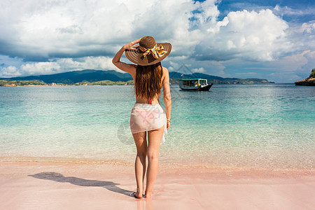 在热带海滩穿着草帽和网目泳裙的有吸引力的年轻女子图片