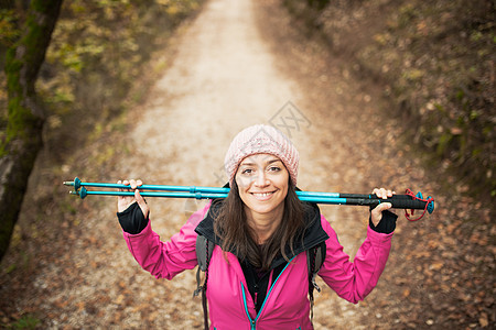 穿粉红色衣服的女孩在森林的一条小路上 看着摄影机 手拿着电线杆 秋天自然 微笑 乐趣图片