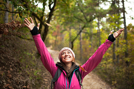 穿着粉红色的少女在森林中漫步 手举起来享受秋天季节自然落叶 微笑 女士图片
