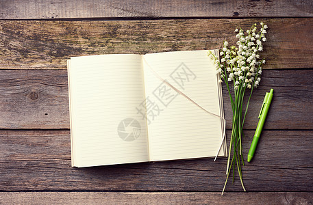 打开的笔记本 上面有空白的白纸和一束盛开的山谷百合花 放在一张木桌上 用灰色的木板做成图片
