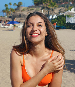 橙色比基尼泳装的美丽的微笑的女孩在热带海滩 快乐的年轻女子在海上微笑的画像 黑发晒黑的女孩穿着泳装在沙滩上享受阳光图片