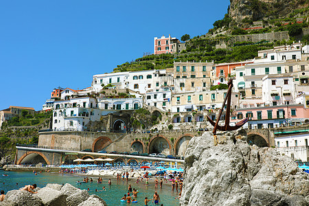意大利阿特拉尼-2018 年 7 月 2 日 在意大利阿马尔菲海岸阿特拉尼的海滩上锚定在石头和人们身上图片