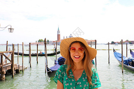 带着墨镜和帽子微笑的女人 看着摄影机 背景上还有威尼斯环礁 夏天 缆车图片