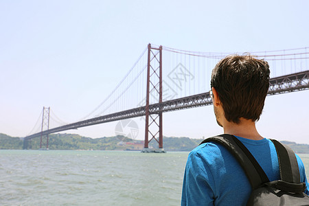 看桥梁的年轻背包客人后面看法 4 月 25 日桥旁葡萄牙里斯本海滨的旅行者或背着背包的游客图片