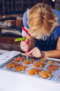 面目全非的女性糖果师用糕点袋手工装饰姜饼人 画上微笑 让它变得可爱 有趣和美味 女人在厨房里做姜饼饼干图片