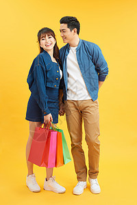 快乐的一对年轻夫妇 带着购物袋拥抱和看着彼此孤立在黄色上图片