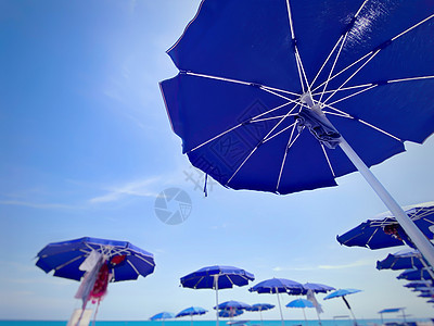 在阳光明媚的夏天 在意大利海滩上排成一排地打开并安排蓝太阳雨伞图片