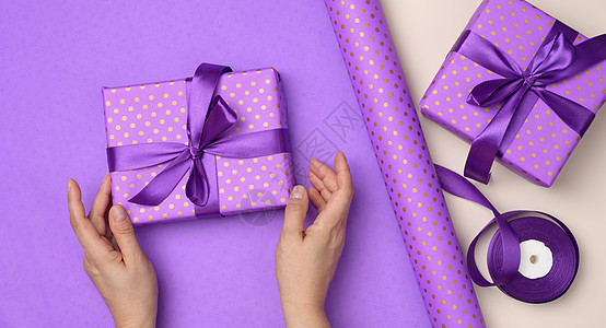 两只女性手拿着紫色礼物盒 在纸面背景上 祝贺的观念在生日 盒子 工作室图片