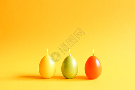传统的复活节装饰 黄色背景上彩蛋形的一组明亮燃烧的石蜡蜡烛 手工制作的图片
