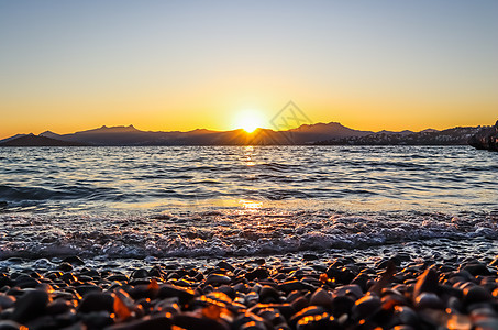 地中海沿岸美丽的夕阳 有岛屿和山丘 阳光照亮的海滩上的石块;以及 黄昏 希腊图片