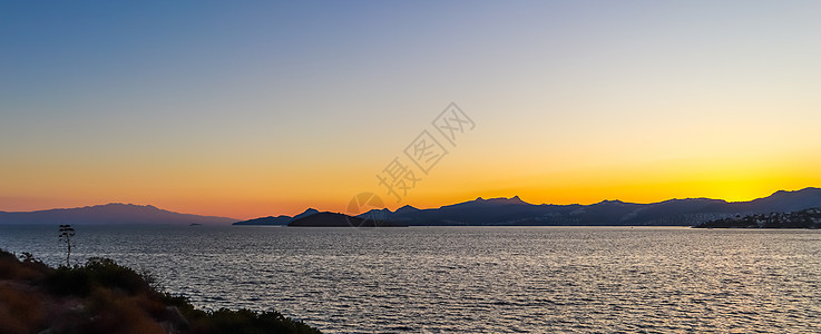 地中海沿岸美丽的夕阳 有岛屿和山丘 阳光照亮的海滩上的石块;以及 反射 自然图片