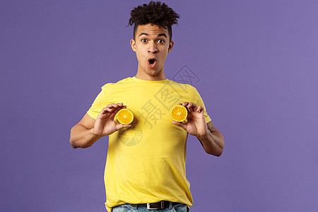 假日 维他命和假期概念 25岁有趣的可爱年轻人的肖像在周围玩耍 胸前用橘子片展示乳房 看起来很羞耻或震惊 紫色背景 投资 工作图片