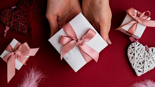 平躺的女人手拿着礼物 盒子上装饰着红色背景的粉红丝带 情人节快乐 圣诞节母亲节 新年 爱图片