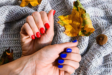 毛衣秋季舒适背景上有蓝色和红色指甲的手 女性修指甲 迷人的美丽修指甲 红色和蓝色的冬季或秋季修指甲图片