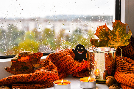有毛衣和鬼南瓜的蜡烛 窗台上的干叶子 万圣节家庭装饰品 雨天窗户 万圣节装饰 燃烧图片