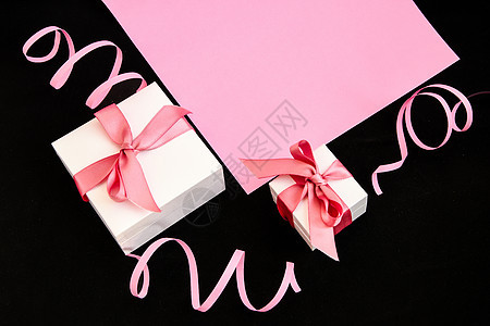 粉色和黑色背景上带有粉色丝带的礼物盒图片