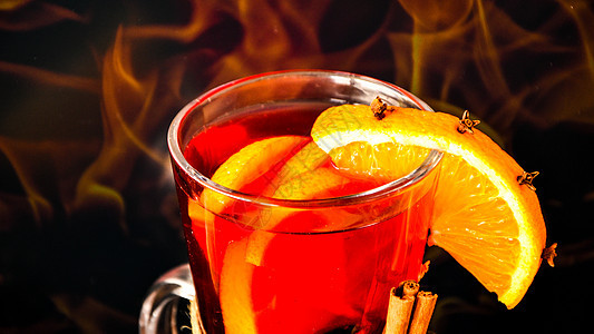 在燃烧的壁炉旁边的玻璃杯里放热味葡萄酒 热圣诞饮料 橙片 肉桂棒 香肠星图片