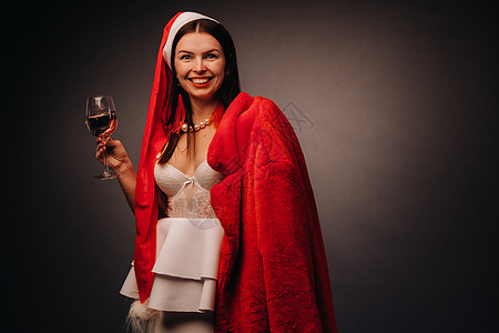 一个戴着圣诞帽和白色裙子的女人 手里拿着玻璃杯和一件红色皮大衣 背景是黑色 圣诞节 假期 美丽的 美丽图片