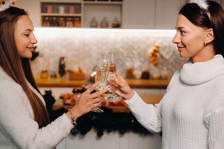 圣诞节时 两个女孩在舒适的家庭环境中 手里拿着香槟 微笑的女孩在节日的夜晚喝香槟 雪姑娘 鸡尾酒图片