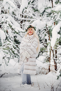 在寒冷的冬天森林里穿着白色皮草大衣的女人的画像 在白雪覆盖的冬季森林里 头戴花环的女孩 白色衣服 裙子图片