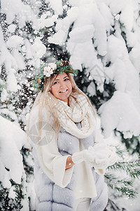 在寒冷的冬天森林里穿着白色皮草大衣的女人的画像 在白雪覆盖的冬季森林里 头戴花环的女孩 头上的花环 新年图片