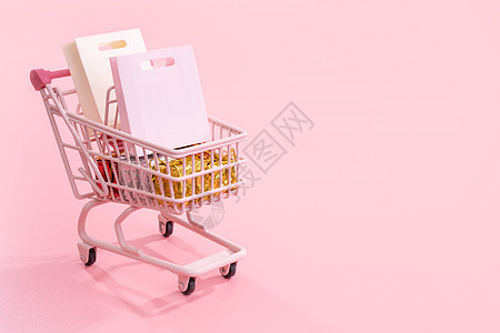 年度销售购物季概念 — 迷你粉色购物车手推车 里面装满纸袋礼物 与淡粉色背景隔离空白复制空间关闭 u 柔和的 购物中心图片