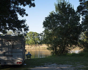 男人坐在法国河堤岸边的露营车旁边图片