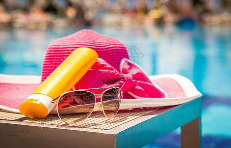在游泳池附近的桌边 装有墨镜和帽子的一瓶日晒奶油图片
