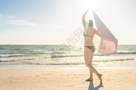 女人拿着毛巾站在沙滩上 还有海在背景上 蓝色的图片