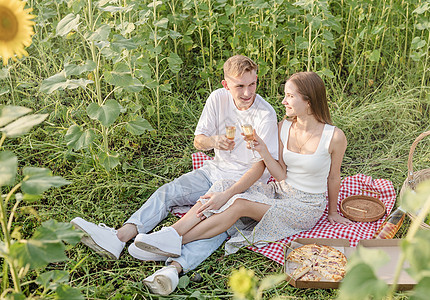 日落时在向日葵田野野餐的年轻夫妇 喝 食物图片
