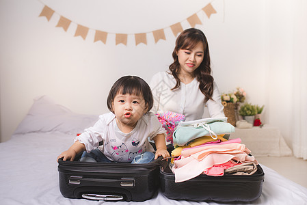 亚洲妈妈和女婴带着手提箱行李和准备度假旅行的衣服 夏天 包装图片