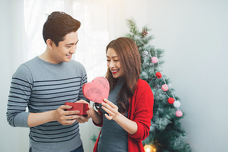 一个英俊的男人 在家里给她的女朋友/妻子一份礼物庆祝新年 人们欢庆的新年 树 迷人的图片