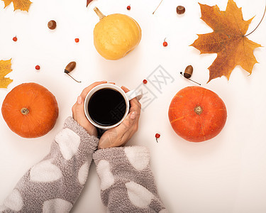 一个女人在白色背景的南瓜黄木瓜叶附近 拿着一杯黑咖啡 秋天平地上躺着 橡子 乡村图片