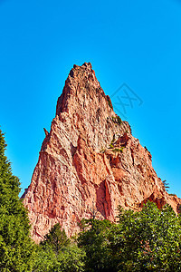 红岩块状红色天空和绿树的三角形大柱图片