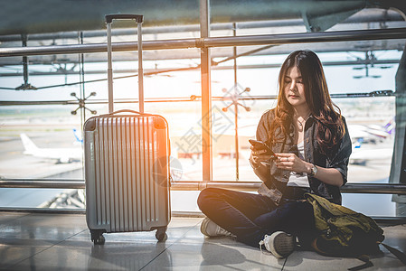 亚洲女性旅客在机场使用智能手机查看航班时刻表 人与生活方式的概念 技术和商业理念图片
