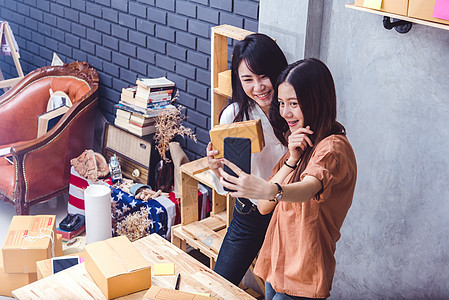 两个女人一起在网上卖东西的时候用手机自拍 商业和人们的生活方式概念 泰国妹子网购时拍照留念图片