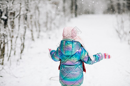 后视笑得开心的孩子 穿着五颜六色衣服和帽子的可爱女孩 在白雪皑皑的冬季公园里奔跑 捕捉雪花 童话冰林中的冬季小女孩 走在冬天的森图片