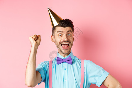 假期和庆祝活动的概念 生日快乐的男孩 留着胡子 戴着领结 戴着派对圆锥帽和节日服装 举手大喊是 吊带裤 男人图片