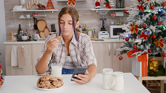 享受冬季节假日的快乐女孩坐在桌边 坐在以xma装饰的厨房厨房桌子上 浏览智能手机图片