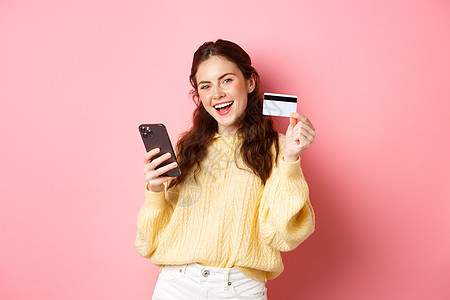 技术和网上购物 快乐而满意的女性客户 展示塑料信用卡并使用手机应用程序在线支付 站在粉红色背景下图片