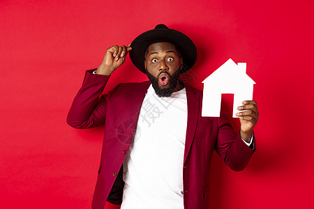 新年广告快乐的黑人男子展示纸屋和微笑 推荐经纪人 站在红色背景之上 注 红色背景 帽子 情感背景