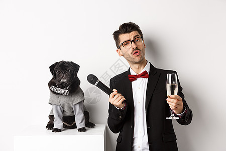 戴眼镜的帅哥 举起香槟杯 给穿着派对服的可爱哈巴狗送麦克风 庆祝和玩乐 白色背景 衣服 微笑图片