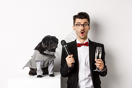 男艺人举杯香槟 给可爱的黑狗麦克风 站在白底背面上站着 戏服 促销图片