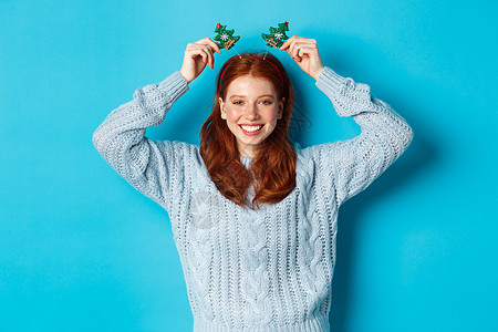 冬季假期和圣诞销售概念 美丽的红头女模特儿庆祝新年 穿着有趣的晚会头带和毛衣 在摄影机上微笑 眼镜 圣诞节图片