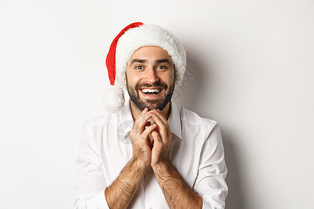 派对 冬季节假日和庆祝概念 在圣塔帽子上兴奋而充满希望的人 带着令人惊叹的白色背景观看圣诞礼物 假期 时尚图片