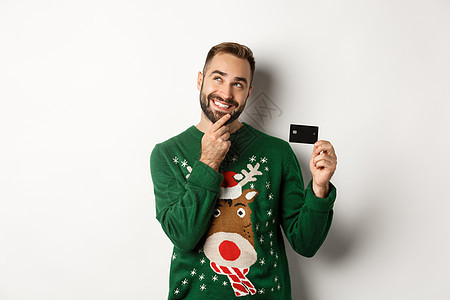 策划新年礼品清单 持有信用卡和微笑 站在白背景之上的深思熟虑的人;在圣诞节假日和购物概念上站立背景图片