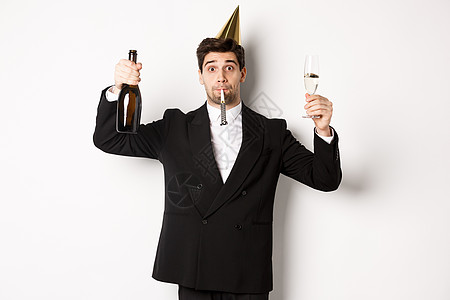 假期和生活方式的概念 帅哥庆祝生日 吹派对口哨 拿着香槟 祝酒 穿着西装站在白色背景中 商务人士 香槟酒图片