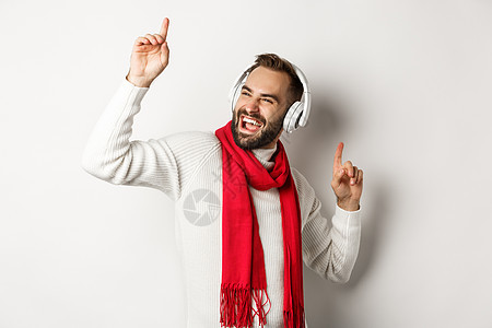 冬季假日和技术概念 快乐的人跳舞用耳机音乐 穿着毛衣站在白色背景的白背面上 成人 购物图片