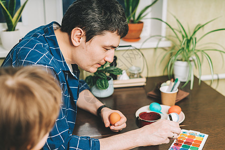 复活节 父亲和儿子在木制背景上画鸡蛋 一家人坐在厨房里 为复活节做准备 创意自创装饰 两个人 家庭图片