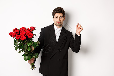 穿着黑色西装的优雅而时髦的男人的形象 看起来自信 手捧红玫瑰花束 正在浪漫约会 站在白色背景下 订婚 快乐的图片